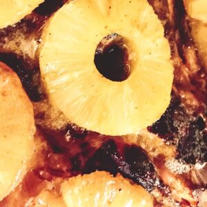Pineapple rings stuck to the side of cooked, somewhat blackened, ham. It's honey holding it in place.
