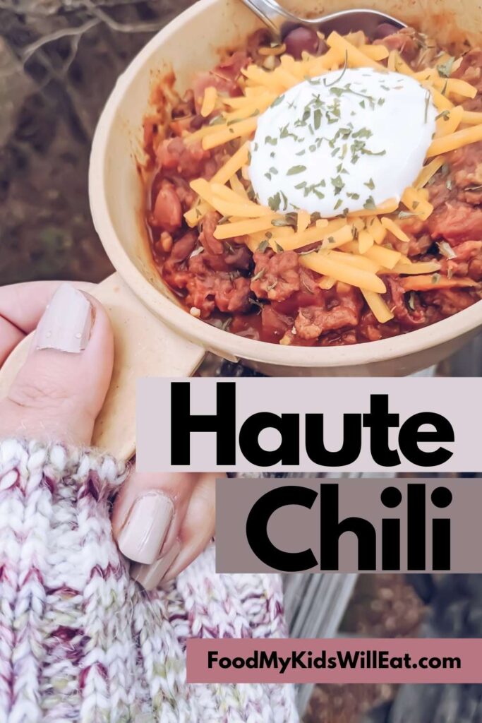 Haute Chili. Yummm. 6 Photograph of hand holding a beige bowl with a thumb-sized handle over wooden fence overlooking fallen autumn leaves and bare trees.