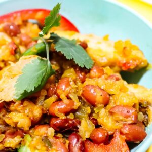Photo of Chicken Lio Caliente in a teal bowl on a yellow plate featuring beans, cauliflower rice, red pepper, green pepper, onion, and cilantro.