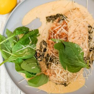 Photo of Chicken Florentine on gray plate with spinach and creamy white wine sauce and parmesan cheese
