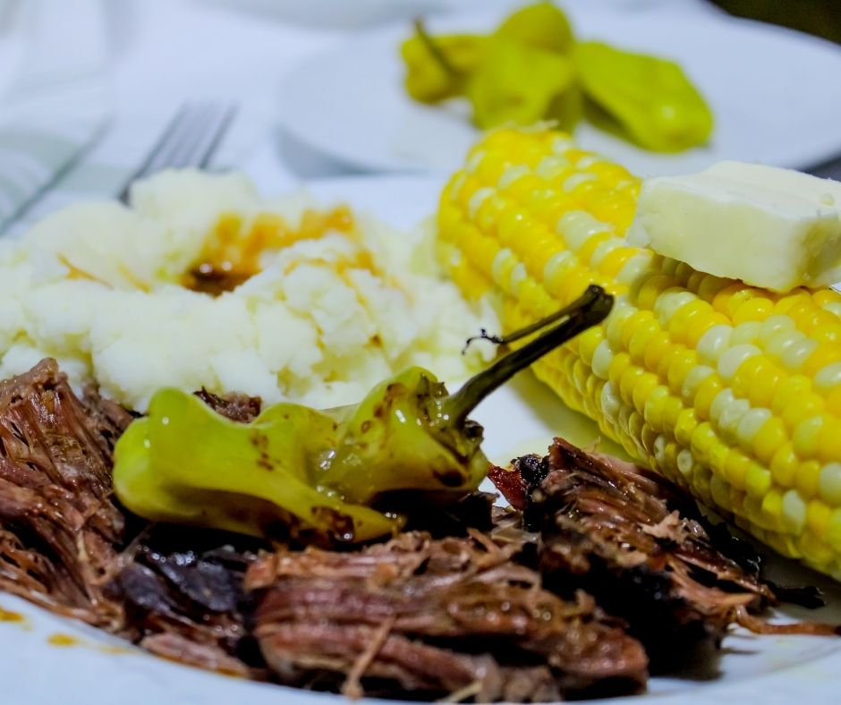 Mississippi Roast with a Pepperoncini Pepper on it served with Mashed Potatoes, Gravy, and Corn on the Cob with Butter.