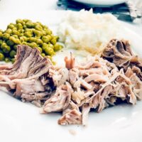Super Easy 3 Ingredient Slow Cooker Pork Roast Recipe 3 Slow Cooker Pork Roast with Sauerkraut, peas, and mashed potatoes on a white plate looking scrumptious.