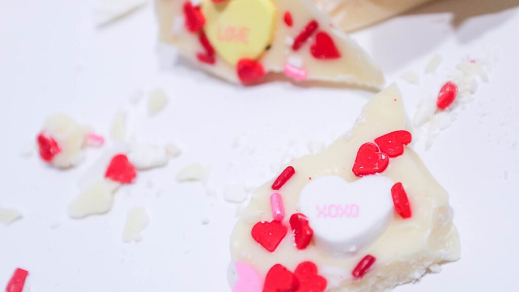 White Chocolate Sweethearts Bark made with love 6 White chocolate bark with conversational hearts and red heart sprinkles scattered about on a white background for a festive Valentine's Day Snack.